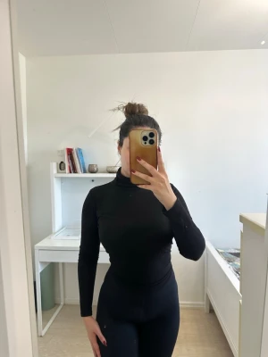 Svart polotopp med lång ärm - Säljer en svart polotopp med lång ärm och tight passform. Toppen är enkel och stilren, perfekt att matcha med olika outfits. Materialet känns mjukt och stretchigt, vilket gör den bekväm att bära hela dagen.