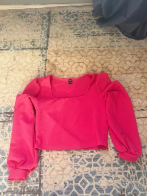 Croppad rosa topp med puffärmar - Säljer en croppad topp i stark rosa färg med puffiga långärmar och fyrkantig ringning. 