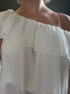 Vit offshoulder blus med volang - Säljer en luftig vit offshoulder blus med volangdetalj. Går att ha på olika sätt Toppen är ärmlös och har en flowy passform som ger en romantisk vibe. Perfekt för varma dagar och enkel att styla med jeans eller kjol. 