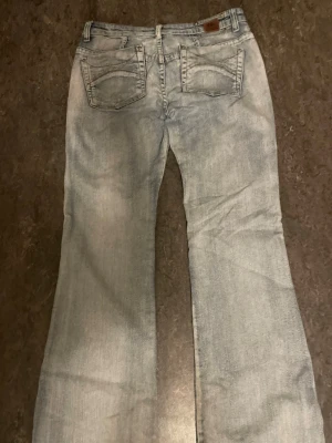 Ljusblå bootcut jeans - Säljer ett par ljusblå bootcut jeans med klassisk femficksdesign och snygg tvätt. Jeansen har normal midja och raka ben som går ut lite nedtill för en retro vibe. Perfekta till sneakers eller boots!