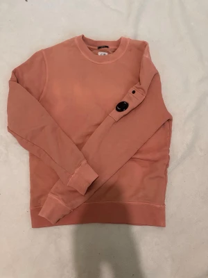 Rosa cp company  - En enkel och stilren rosa sweatshirt med rund hals och långa ärmar. Tröjan har ribbade muddar vid ärmslut och nederkant. Perfekt för en avslappnad och trendig look.
