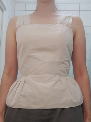 Beige peplumtopp med breda axelband - Säljer en beige topp med breda axelband och markerad peplum midja, i styvt elegant tyg. Toppen har en enkel, stilren design med lätt rynkade detaljer vid midjan som ger en snygg peplumsiluett. Perfekt att matcha med jeans eller kjol för en clean look, eller kostymbyxor för en fin middag. Se mått på bilder och se gärna mina andra annonser <3