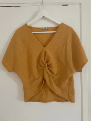 Gul topp  - Trendig gul croppad topp med v-ringning och twistad detalj framtill. Toppen har korta ärmar och är tillverkad i ett mjukt, ribbat material som ger en avslappnad men snygg look. Perfekt att styla med höga jeans eller kjol.
