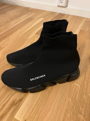 Balenciaga Speed Trainer svarta sneakers - Svarta Balenciaga Speed Trainer sneakers med stickad ovandel i stretchigt tyg och tjock, futuristisk sula. Modellen har en sockliknande passform och vit Balenciaga-logga på sidan. Perfekta för dig som gillar streetwear och vill ha något trendigt. Dom har blivit lite smutsiga och lite mer använda men annars är d bra