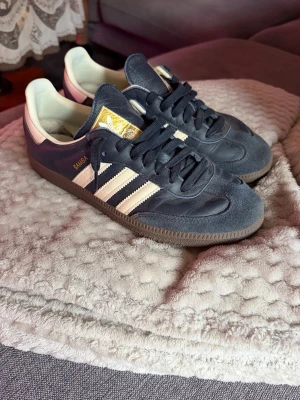 Adidas Samba  - Klassiska Adidas Samba sneakers i den eftertraktade blåa färgen, mocka och läder med vita detaljer och gummisula. Skorna har de ikoniska tre ränderna på sidan och gulddetaljer på plösen. Lågt skaft och tidlös retrostil som funkar till det mesta. Köpta på FootLocker i Barcelona, box+vita snören tillkommer! Inte använda många gånger så bra skick! Strl 42 2/3