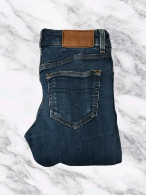 Tiger Of Sweden Mörkblåa Jeans - Snygga mörkblå jeans med klassisk femficksdesign och raka ben. Jeansen har en brun läderpatch i midjan och kontrastsömmar. Perfekta för en avslappnad och trendig look. Tillverkade i denim med en skön passform. W28 L32