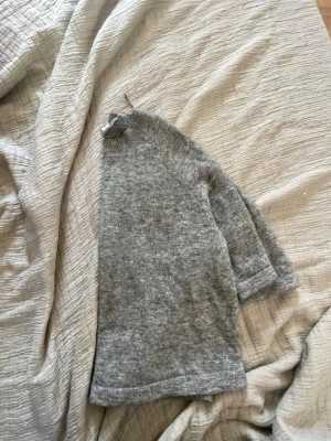 Grå stickad tröja med kort ärm - Mysig grå stickad tröja med korta ärmar och rund hals. Tröjan har en avslappnad passform och är gjord i ett mjukt material som känns skönt mot huden. Perfekt att styla med jeans eller kjol för en chill look.
