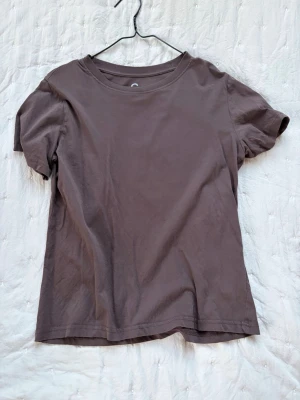 Brun basic t-shirt i bomull - En enkel brun t-shirt i mjuk bomull med rund hals och korta ärmar. Passformen är normal och tyget känns skönt mot huden. Perfekt till jeans eller shorts för en avslappnad look.