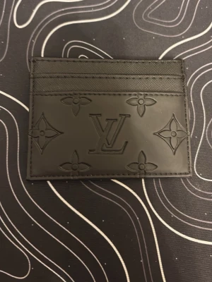 Plånbok - Snyggt svart kortfodral med präglad monogramdesign. Fodralet har flera kortfack och är gjort i slätt läder med stilrena detaljer. Perfekt för dig som vill ha en smidig och lyxig accessoar i fickan.