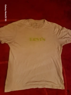 Beige Levi's t-shirt i bomull - Säljer en beige t-shirt från Levi's med klassisk logga i grönt framtill. T-shirten är i mjuk bomull och har en normal passform med korta ärmar och rund hals. Perfekt till jeans eller shorts för en enkel och clean look.