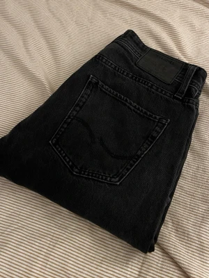 Relaxed/Chris jeans från Jack & Jones - Säljer ett par svarta jeans med rak passform och klassisk femficksdesign. Jeansen har en enkel bakficka och är tillverkade i kraftigt denimtyg. Perfekta för en clean och stilren look.