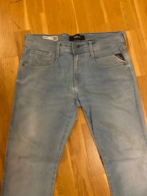 Ljusblå jeans från Replay - Snygga ljusblå slim fit jeans från Replay med klassisk femficksmodell och diskreta slitningar. Jeansen har en smal passform och är tillverkade i ett mjukt denimtyg som ger en bekväm känsla. Perfekta för en avslappnad och trendig look.