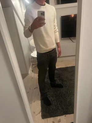 Vit rundhalsad tröja Uniqlo - Säljer en stilren vit tröja från Uniqlo med rund halsringning och långa ärmar. Tröjan har en enkel och clean design, perfekt att matcha med jeans eller chinos. Tillverkad i mjukt material som känns skönt mot huden.