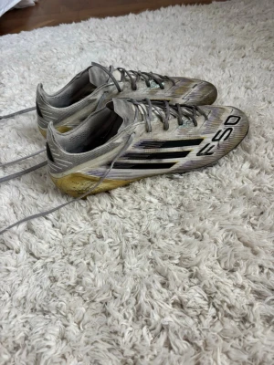 Adidas F50 fotbollsskor silver/guld elite - Säljer ett par Adidas F50 fotbollsskor i bra skick lite små repor här och där man inget man tänker på. Påse saknas därför säljer jag dom billigt, kan lösa ett par extra sulor om det skulle önskas. Hör av dig för fler frågor eller bilder! (Storlek 43 1/3)