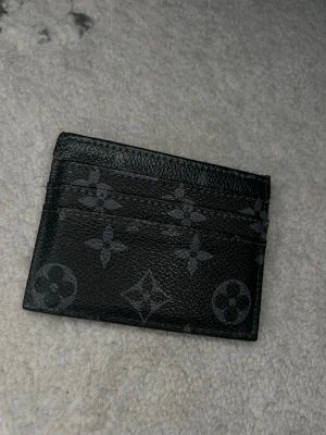 L V - Snyggt svart kortfodral  med klassiskt monogrammönster i grått. Tillverkat i slittåligt läder och har flera fack för kort. Perfekt för dig som vill ha en stilren och exklusiv accessoar i fickan.
