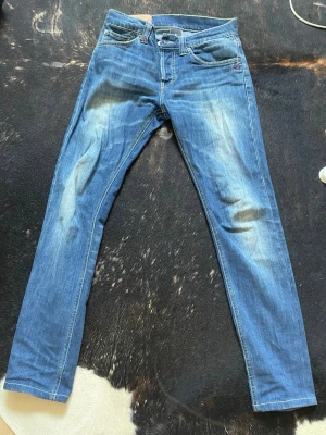 Dundup jeans - Snygga blå slim fit jeans med ljusa slitningar framtill och på bakfickorna. Klassisk femficksmodell med dragkedja och knapp i midjan. Jeansen har raka ben och är tillverkade i ett mjukt denimtyg som ger en avslappnad look.