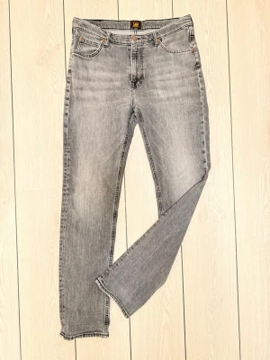 Grå tvättade Lee jeans - Säljer ett par grå tvättade jeans från Lee med klassisk femficksmodell och raka ben. Jeansen har en snygg vintagekänsla och Lee-logga bak i midjan. Perfekta för dig som gillar en avslappnad och trendig streetwear stil.