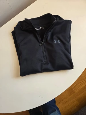 Svart ColdGear tröja från Under Armour - Säljer en svart långärmad ColdGear-tröja från Under Armour med halv dragkedja och hög krage. Perfekt för träning eller utomhusaktiviteter när det är kallt. Tillverkad i ett tekniskt material som håller dig varm och torr.