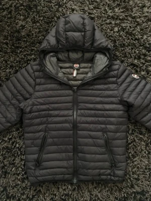 Svart dunjacka från Colmar - Snygg svart dunjacka från Colmar med huva och två dragkedjeförsedda fickor. Jackan har quiltad design och Colmar-logga på ärmen. Perfekt för kalla vinterdagar och riktigt skön att bära.