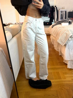 Vita raka jeans med hög midja - Säljer ett par vita jeans med rak passform och hög midja. Jeansen har klassisk femficksdesign och stängs med knapp och dragkedja. Materialet är kraftigt och ger en snygg siluett. Perfekta till en trendig och avslappnad look.