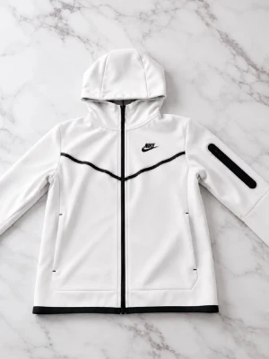 Vit nike tech - Snygg vit hoodie från Nike med svart dragkedja och svarta detaljer. Hoodien har en huva, två fickor framtill och en cool svart linje över bröstet. Nike-logga på vänster sida och en extra ficka på ena ärmen. Perfekt för en sportig och avslappnad stil.
