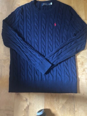 Polo Ralph Lauren kabelstickad tröja Navy M - Mörkblå kabelstickad tröja från Polo Ralph Lauren i storlek M. Tröjan är i mycket fint skick utan några defekter, fläckar eller missfärgningar. Jag säljer den endast eftersom den är lite för liten för mig. För referens är jag 182 cm lång och väger cirka 68 kg. Hör gärna av dig om du har några frågor eller vill se fler bilder. Pris kan diskuteras vid snabb affär.