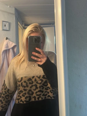 Beige och svart leopardmönstrad tröja - Säljer en snygg beige och svart tröja med leopardmönster över bröstet och ärmarna. Tröjan har en avslappnad passform och långa ärmar. Perfekt för dig som vill sticka ut lite extra med ett djurmönster.