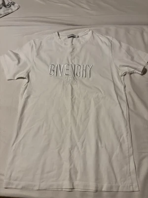 Vit Givenchy Paris t-shirt - Säljer en clean vit t-shirt från Givenchy Paris med broderad logga framtill. Klassisk rund halsringning och korta ärmar. Tillverkad i mjuk bomull för skön känsla och stilren look. Perfekt för dig som gillar exklusiva streetwear-plagg.