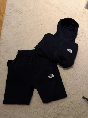 Mörk blått set från The North Face - Säljer ett mörk blått set från The North Face med luvtröja, shorts och byxor. Alla delar har dragsko i midjan och logga på vänster sida. Materialet är mjukt och bekvämt, perfekt för chill dagar eller träning.