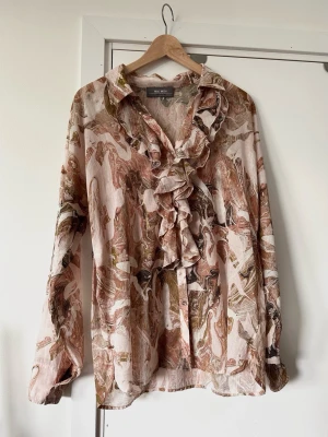 MOS MOSH - Women's Marble Print Ruffle Blouse - size L - Härlig flerfärgad luftig mönstrad skjorta / blus från MOS MOSH i storlek 40, i den populära 'Jelena'-modellen. Tidlös design med långa uppvikbara ärmar och v-ringad krage kantad av fina volangdetaljer. Skjortan har en genomgående knappslå framtill med stilfulla guldfärgade knappar, likaså vid ärmsluten. Vackert marmormönster i rosa, brunt grönt och beige. Litet diskret guldfärgat emblem med Mos Mosh loggan i nacken. Luftigt finvävt tyg i 100% bomull, så bra naturmaterial som andas. Nypris 1490:-