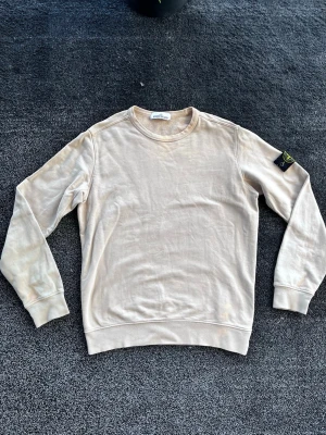 Stone Island sweatshirt - Säljer en beige sweatshirt från Stone Island med klassisk rund hals och ribbade muddar. Tröjan har den ikoniska Stone Island-loggan på vänster ärm och är tillverkad i mjukt bomullsmaterial. Perfekt för en avslappnad och stilren look. Storlek L, äkta, skick 7/10 har några missfärgningar. Pris går att diskutera✅