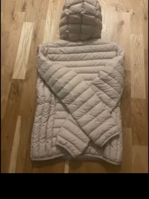 Beige dunjacka med huva - Snygg beige dunjacka med huva och dragkedja framtill. Jackan har quiltad design med horisontella sömmar och två sidofickor. Perfekt för kyliga dagar och enkel att matcha med olika outfits.