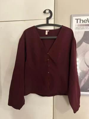 Vinröd blus med v-ringning - Stilren vinröd blus med v-ringning och knappar framtill. Blusen har långa ärmar och är tillverkad i ett tunt, mjukt tyg som ger ett snyggt fall. Perfekt att matcha med både jeans och kjol för en trendig look. Aldrig använd 