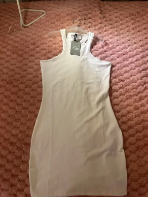Vit ribbad kort klänning H&M - Säljer en vit ribbad kort klänning från H&M i 95% återvunnen polyester. Klänningen har en ärmlös design med breda axelband och rund halsringning. Perfekt för en enkel och stilren look.