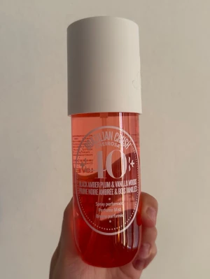 Sol de Janeiro Brazilian Crush Cheirosa 40 - En parfymmist i en cylinderformad plastflaska med vit kork och rosa-orange vätska. Doften är Black Amber Plum & Vanilla Woods och flaskan har en modern, ungdomlig design med tydlig text framtill. Endast testsprutad. 240 ml. 