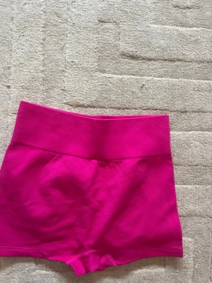 Högmidjade rosa seamless shorts - Säljer ett par knallrosa högmidjade seamless shorts med tight passform. Shortsen har bred resår i midjan och scrunch-detalj bak för extra form. Perfekta för träning eller chill dagar.