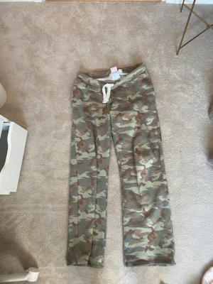 Camo mjukisbyxor från Gina Tricot - Säljer ett par camouflagemönstrade mjukisbyxor från Gina Tricot i storlek L. Byxorna har dragsko i midjan och är tillverkade i mjukt, bekvämt material. Perfekta för chill dagar eller när du vill ha en avslappnad look. 