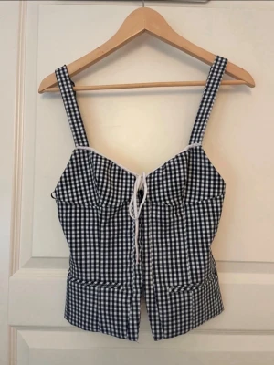 Rutig korsettopp med snörning - Snygg svartvit rutig korsettopp med breda axelband och snörning framtill. Toppen har en figurnära passform och är perfekt för att lyfta vilken outfit som helst. Tillverkad i bomull för en skön känsla.