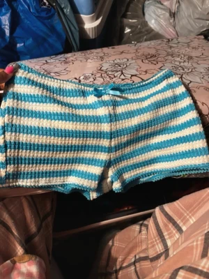 Randiga stickade shorts med rosett - Säljer ett par mysiga stickade shorts med blå och vita ränder. Shortsen har en liten rosett framtill i midjan och är perfekta för chill dagar hemma. De är mjuka och har en relaxed fit som gör dem superbekväma.