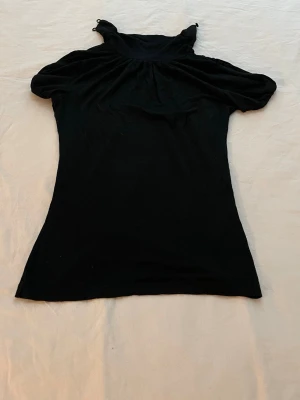 Svart topp med hög krage - Svart topp med hög krage och korta puffärmar. Tunn och mjuk i materialet, perfekt för dig som gillar en enkel men ändå trendig look. Passformen är normal och toppen har en lätt rynkning vid axlarna för extra stil.