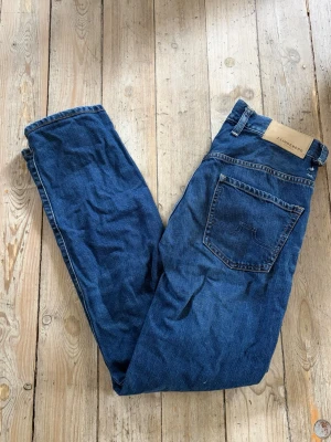 J.Lindeberg Jeans - Säljer dessa blåa J.Lindeberg jeans som är i storlek 30/32 men är uppsydda så de är som 30/30. Jeansen har en straight fit. Jeansen är i bra skick men har en tråkig skada där en bälthållare har tappat fästet, se på bild. Hör av er vid några som helst funderingar!