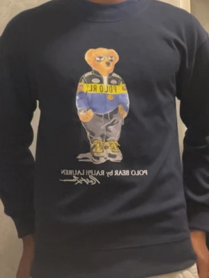 Mörkblå sweatshirt Polo Bear - Säljer en mörkblå sweatshirt från Ralph Lauren med den ikoniska Polo Bear-trycket på bröstet. Tröjan har rund halsringning och långa ärmar. Perfekt för dig som gillar streetwear och vill ha en klassisk men lekfull look.