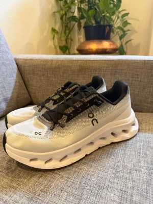 Vita On cloud Running sneakers med svart detalj - Snygga vita sneakers från On Running med svarta detaljer och unik sula med hål för extra dämpning. Ovandelen är i mesh för bra andningsförmåga och skorna har svarta snören. Perfekta för dig som gillar sportig och modern stil.