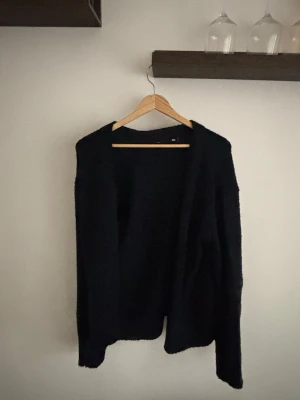 Svart öppen kofta i mjukt material - En mörkblå, öppen kofta med lång ärm och avslappnad passform. Koftan är gjord i ett mjukt och fluffigt material som känns skönt mot huden. Perfekt att slänga på sig över en t-shirt eller topp för en chill look.