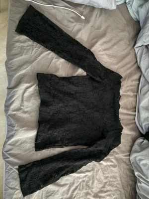 Svart spetsblus från Vero Moda - Snygg svart långärmad blus från Vero Moda i genombruten spets. Blusen har en feminin och elegant look med raka ärmar och rundad hals. Perfekt att styla med jeans eller kjol för en trendig outfit.