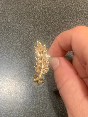 Guldfärgad earcuff i bladform - Snygg earcuff i guldfärgad metall formad som en kvist med blad och en liten rosett längst ner. Örhänget är cirka 4 cm lång och 1,5 cm bred.  har en elegant, glansig finish som ger ett stilrent intryck. Använd vid ett tillfälle och är i väldigt bra skick 