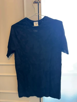 Svart camo t-shirt från ICIW - Snygg svart t-shirt från ICIW med diskret camouflagemönster. Klassisk passform med korta ärmar och rund hals. Perfekt för dig som gillar stilrena träningskläder med en twist.