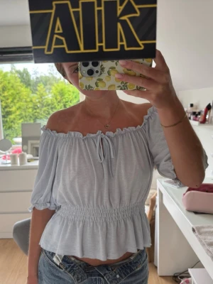 Ljusblå offshoulder blus - Supersöt ljusblå blus med offshoulder. Toppen har lite puffiga ärmar, smock i midjan och en liten knytning framtill. Basic men ändå söt topp som passar till allt🩵 nypris: 299kr