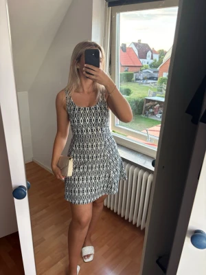 Kort sommarklänning - Kort klänning med blåvitt grafiskt mönster och smala axelband. Klänningen har en figurnära överdel och utställd kjol, perfekt för varma dagar. Materialet ser lätt och bekvämt ut, och modellen har en modern, ungdomlig stil. Aldrig använt.