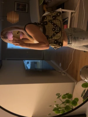 Beige handväska med G-detaljer - Cool beige handväska med bruna detaljer och silverfärgade nitar. Väskan har ett stort G-spänne framtill och mönster med G-bokstäver över hela ytan. Två rejäla handtag och en ficka framtill. Perfekt för dig som gillar statement-accessoarer. Köptes på en marknad
